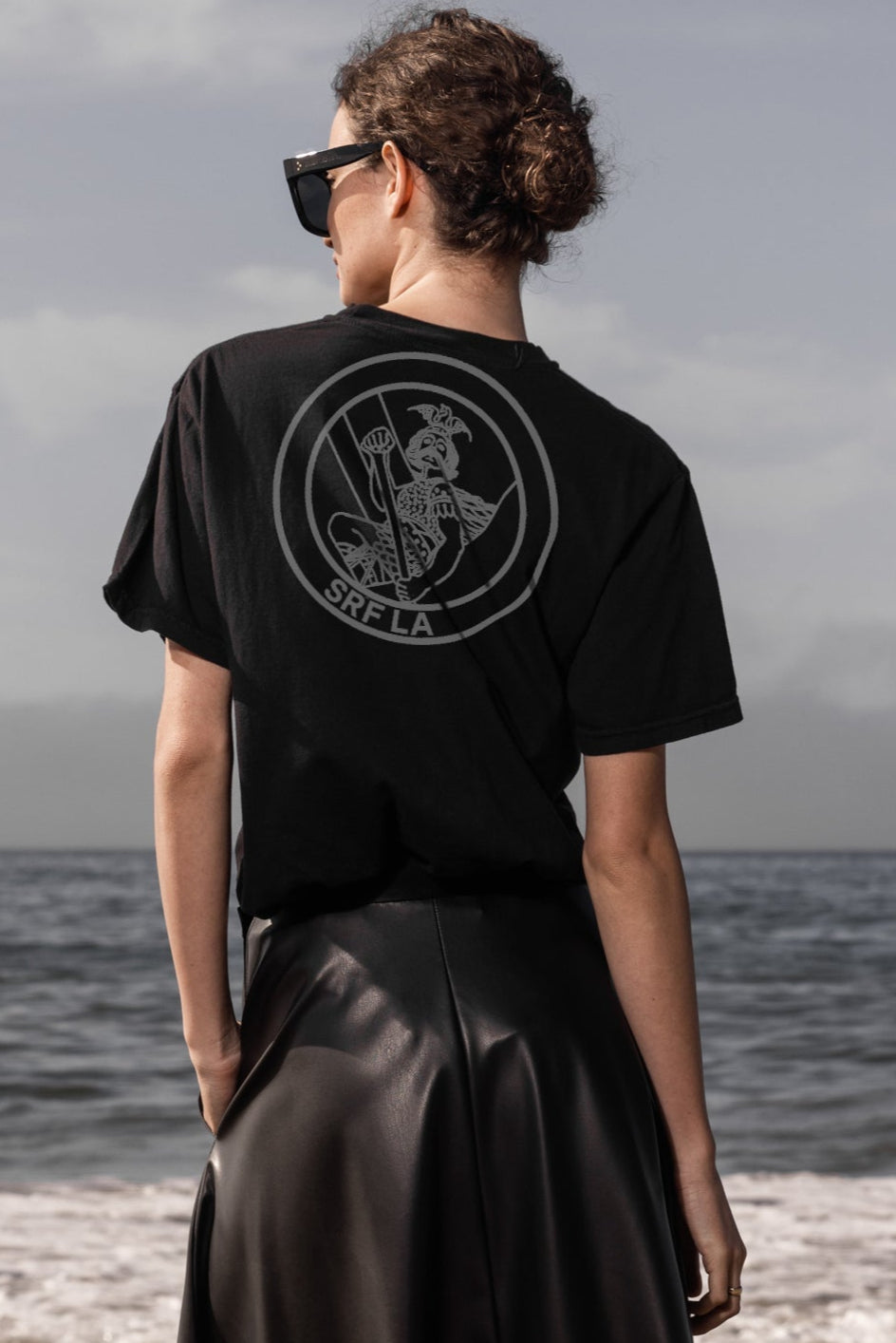 Person wearing a black t-shirt with a logo on the beach