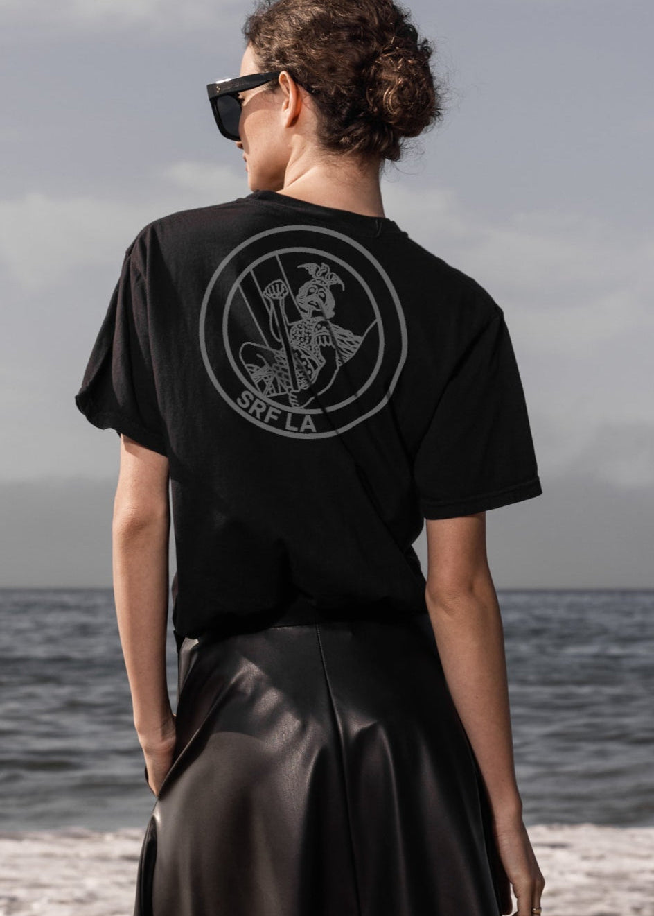 Person wearing a black t-shirt with a logo on the beach